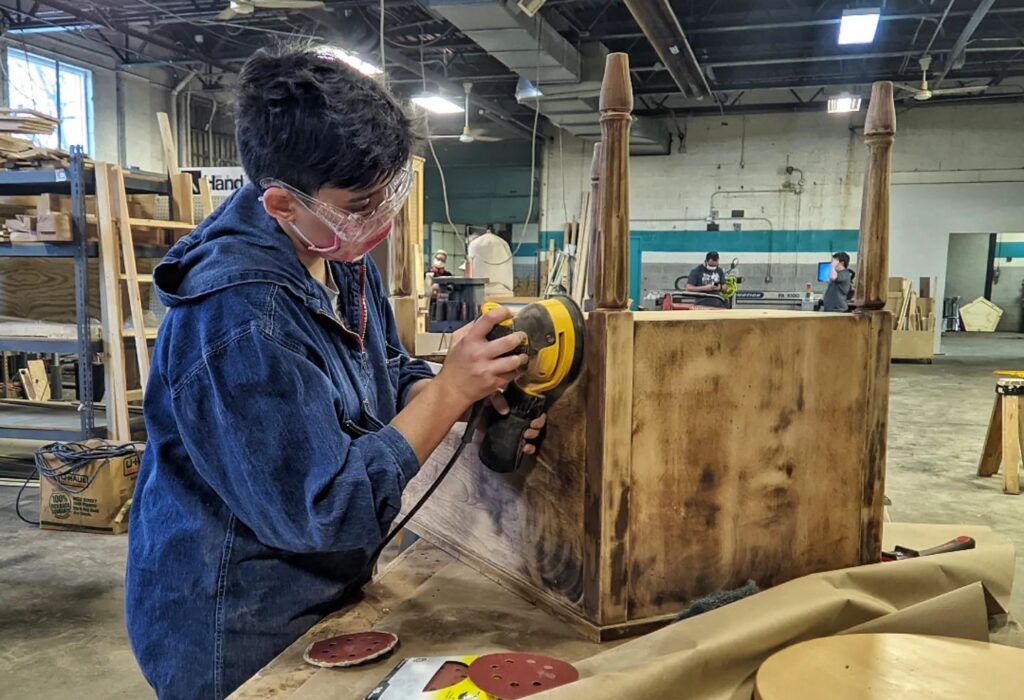 A person with light skin tone sanding a piece of furniture.