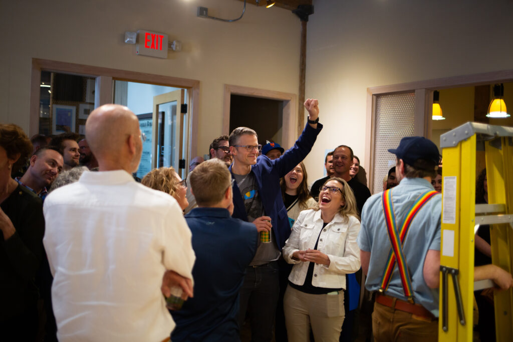 A person raising an arm in the air as other people around look on smiling.