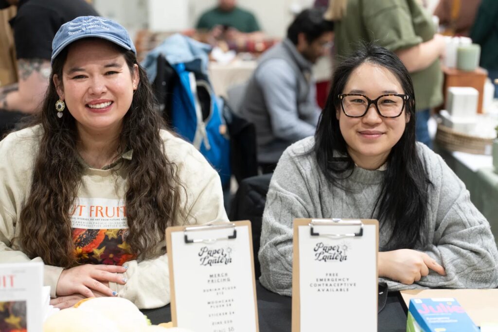 Two smiling people of medium light skin tone sitting at a table.