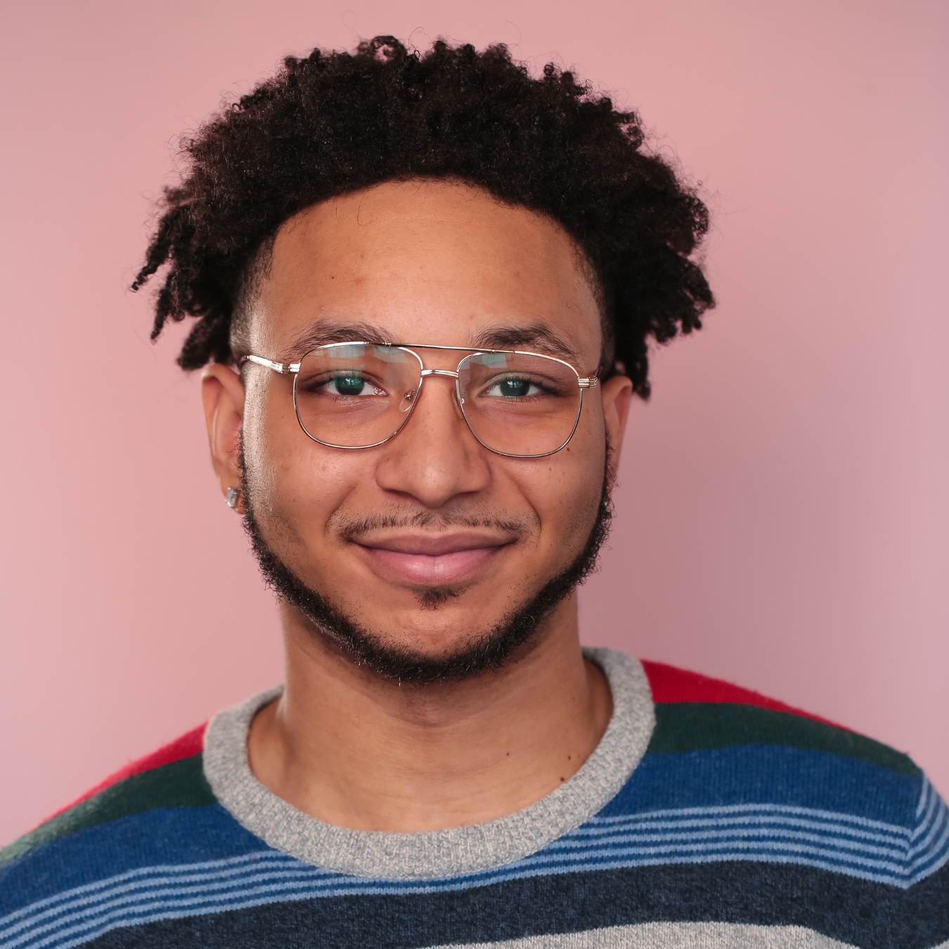 Headshot of a person of medium skin tone with curly black hair, glasses, and a thin mustache and beard.