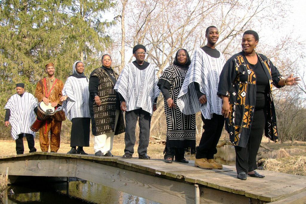 Anita Singleton-Prather and the Gullah Kinfolk, a dynamic gospel group from Gullah, stand and pose in a line on a wooden bridge.