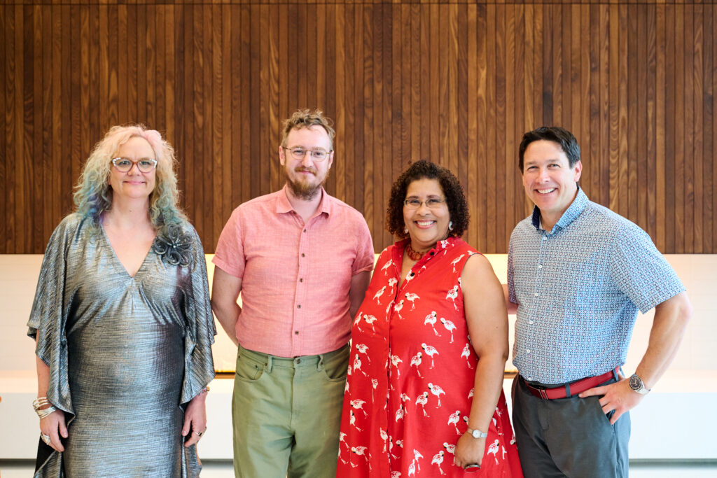 Four smiling people standing in front of a wooden wall.