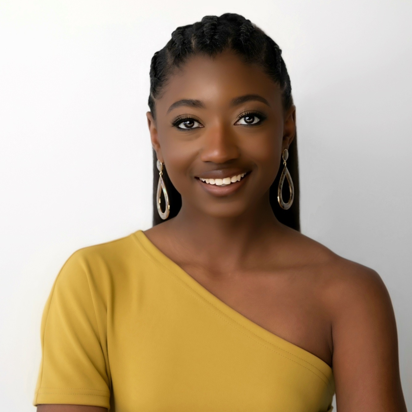 Headshot of a person of dark skin tone with long black hair, gold earrings, and a yellow blouse.