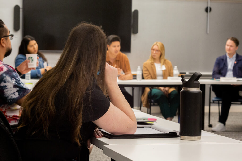 People sitting at long tables listening to speakers.