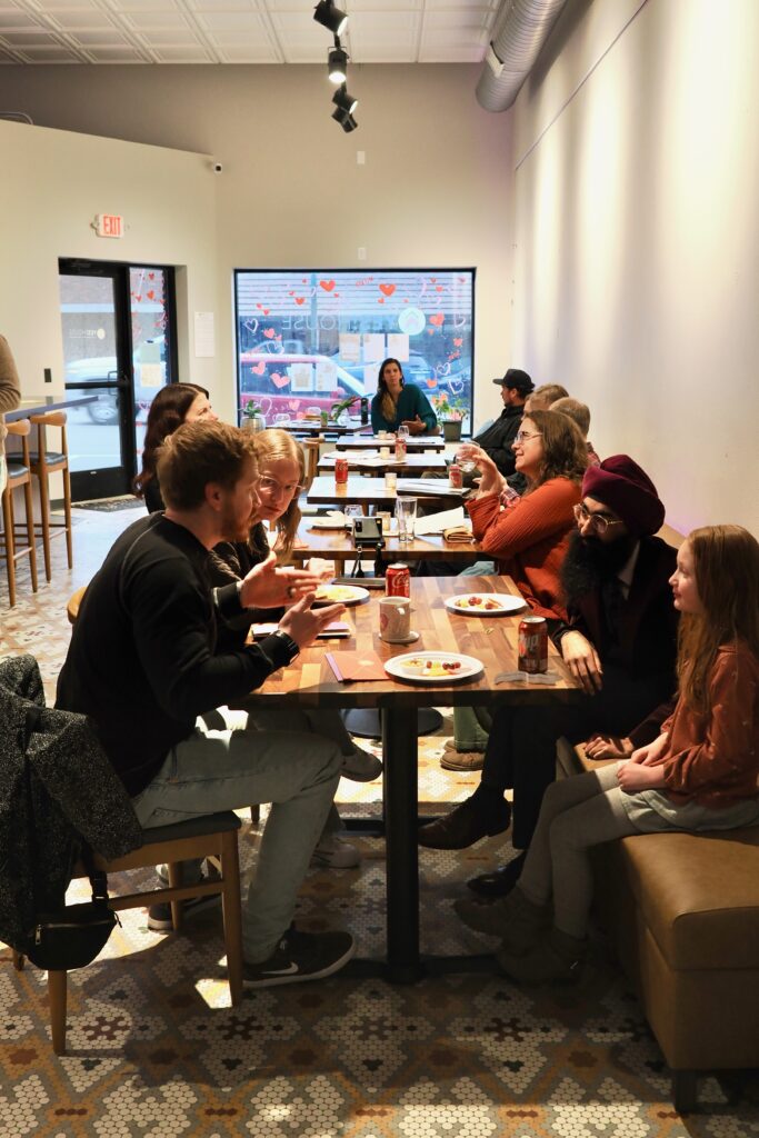A group of people in a friendly warm space filled with tables and chairs.