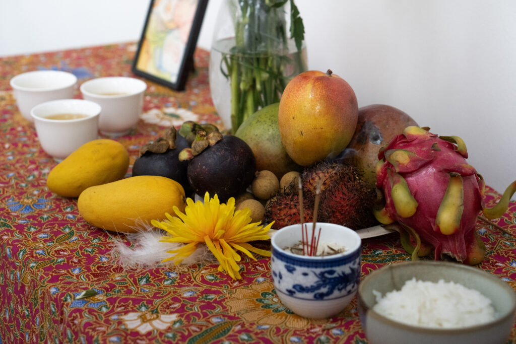 A tableclothed altar featuring fruit, rice, tea, and other objects.