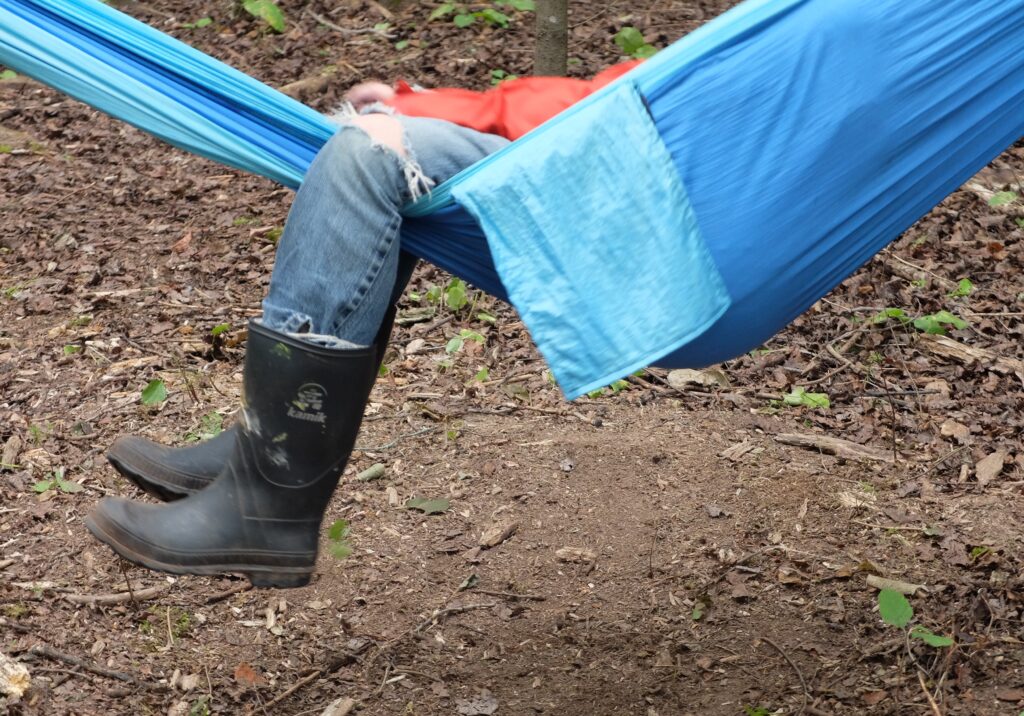 Two legs wearing boots poking out of a blue hammock.