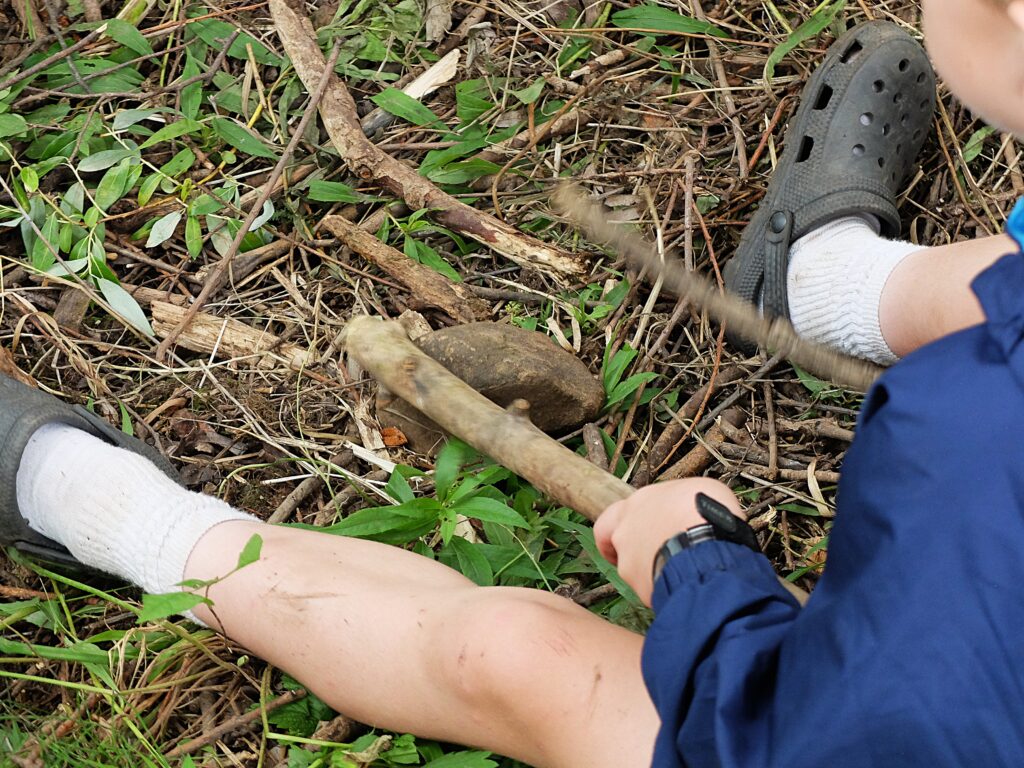 A boy banging sticks on a rock.