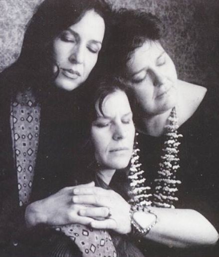Three women close their eyes and embrace each other in a black and white photograph.
