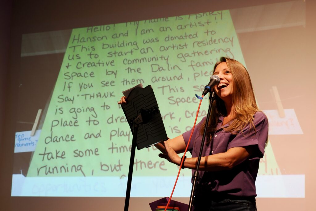 A person with light skin and blonde hair reads a love letter, with a projected green letter behind her.