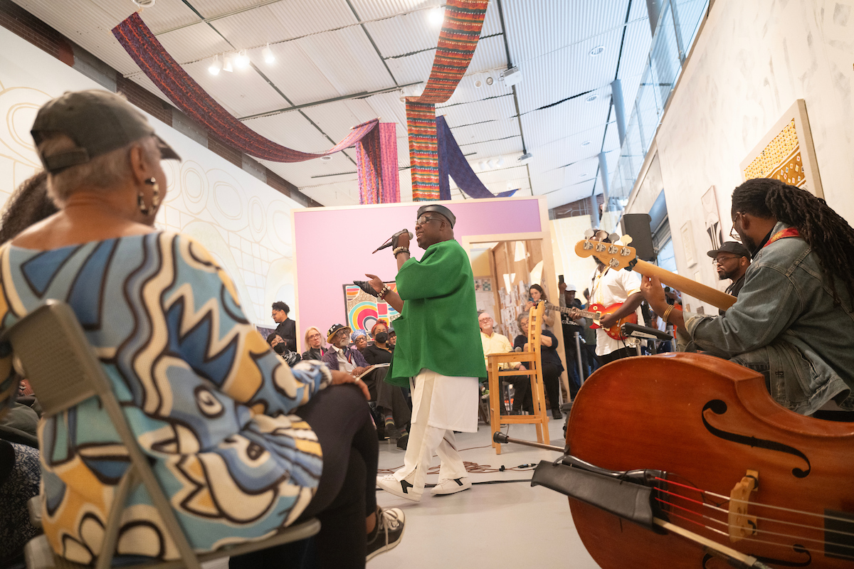 An African American musician encircled by musicians and audience members.