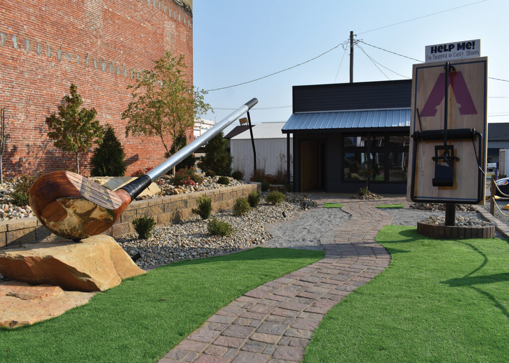 A large golf club sculpture and a large mouse trap sculpture sitting outside next to a building.