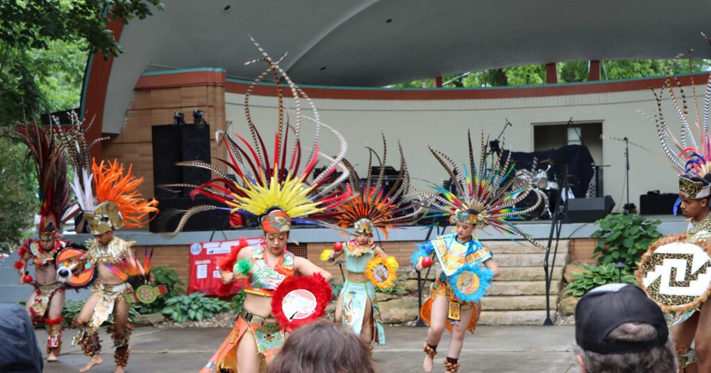 Dancers in aztec garb and feathers perform in an outdoor amphitheater