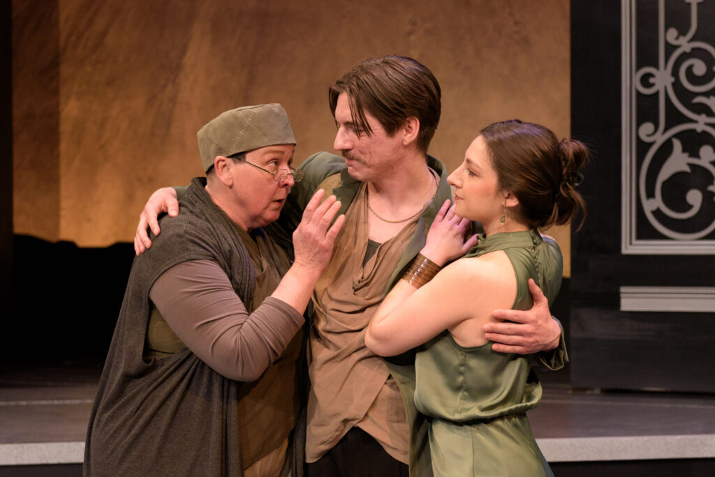 Three people dressed in theatre costumes embracing on stage.