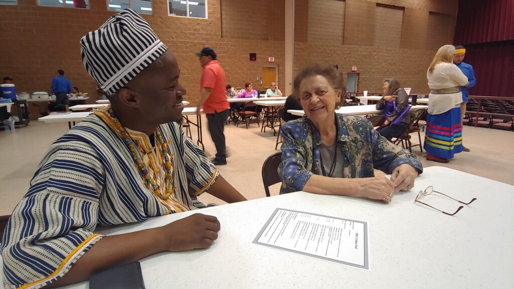 Two smiling people sit together at a table in an auditorium.