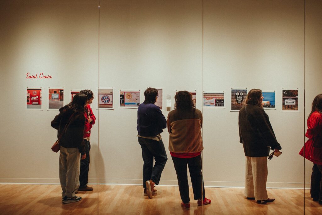 Six people stand and look at images of signs on a white gallery wall.