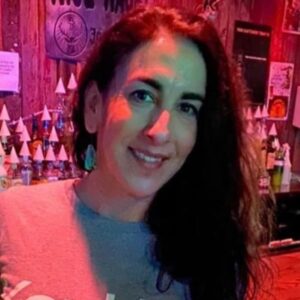 A person with light skin and dark long hair smiles for the camera