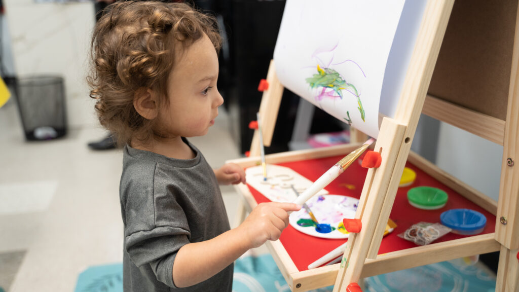 A young toddler looks intent as they paint on an easel.