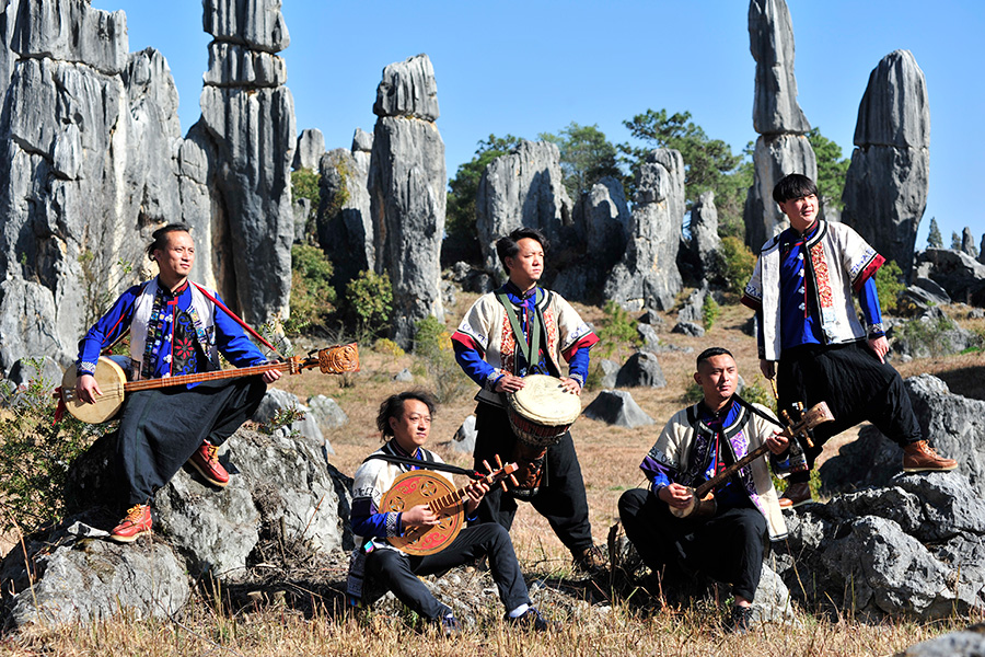 Manhu, a band based in China who brings to life the traditions of the Yi people, pose with various musical instruments amongst a rock formation outside.