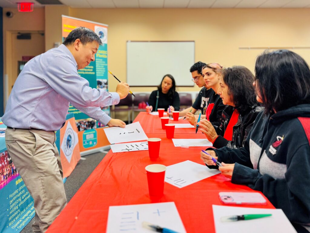 A smiling person leading a group in a callligraphy lesson.
