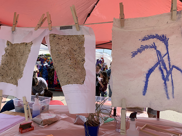 Three pieces of cloth-like paper with designs in the middle hang via clothespins over a table.