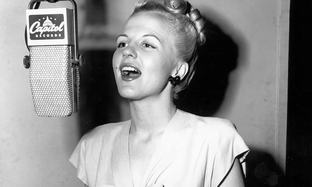 A black and white image of a light-skinned woman singing into a microphone.