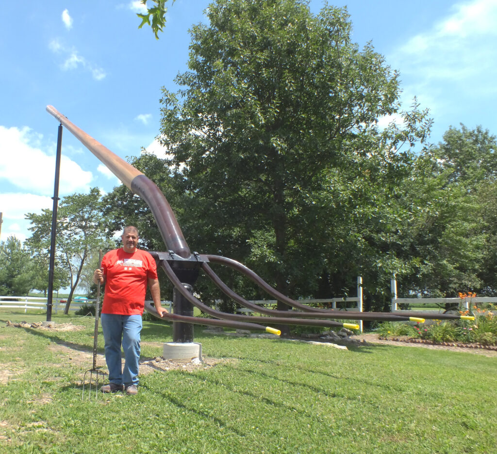 A person standing in front of a giant sculpture of a pitchfork facing down.
