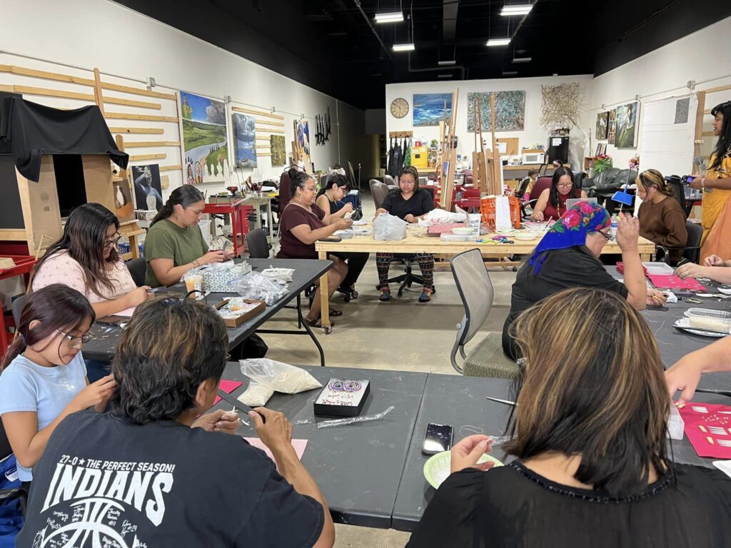 A group of women create shell jewelry at a large table set in a circle