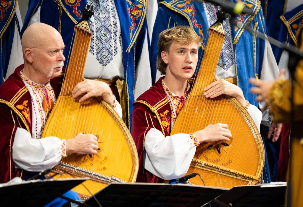 Two light-skinned men play instruments sitting down.