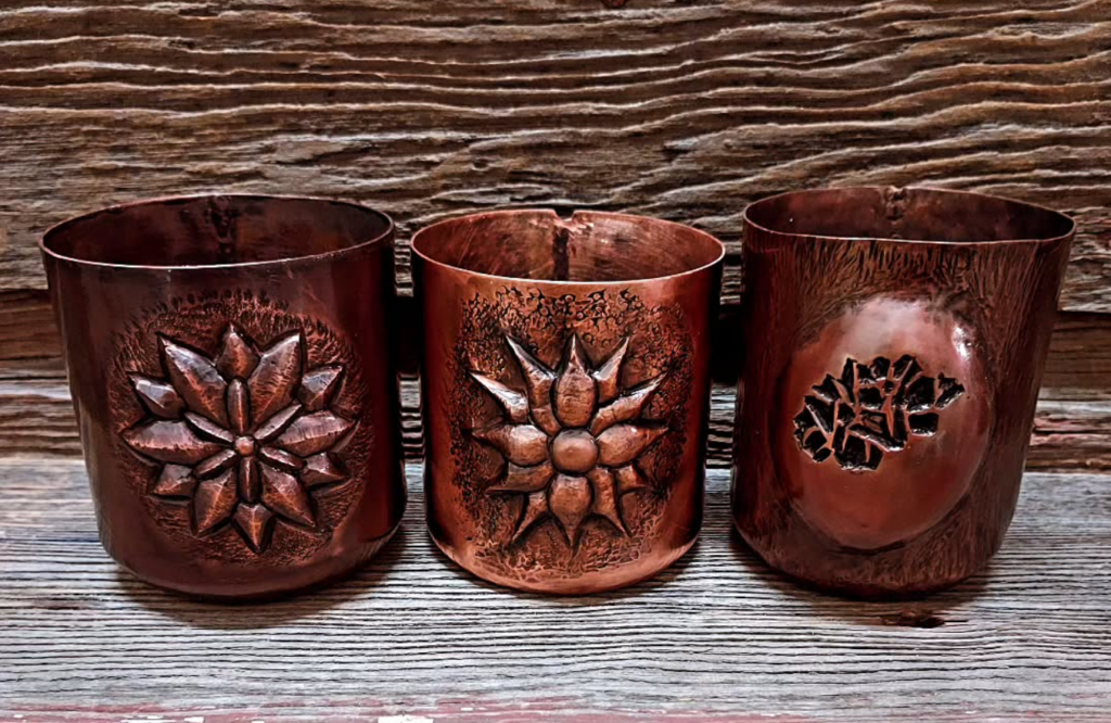 Three decorated copper cups on a table.