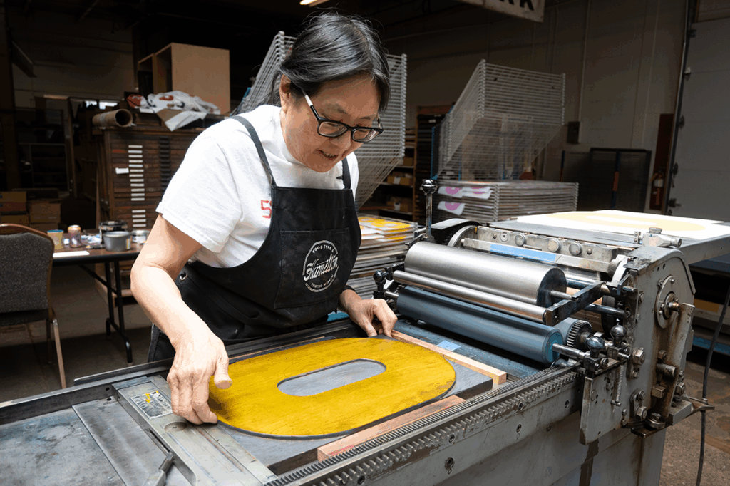 A person letterpress printing a large wood type O