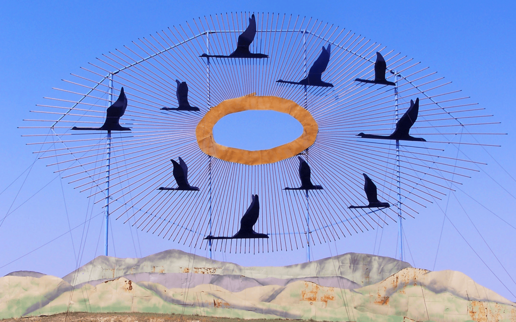 A sculpture of birds, an orange circle and hills against a blue sky.