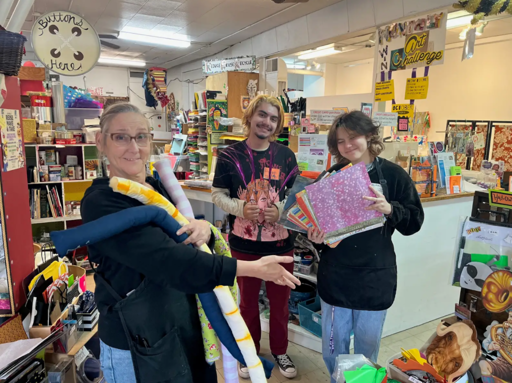 Three people hold items in a shop.